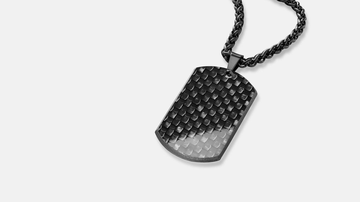 Carbon-Dogtag von Kohlenstoff 12 mit gewebter Struktur und schwarzer Edelstahlkette auf hellem Hintergrund